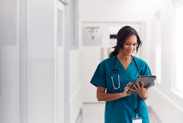A black woman looking at a tablet in her nursing uniform